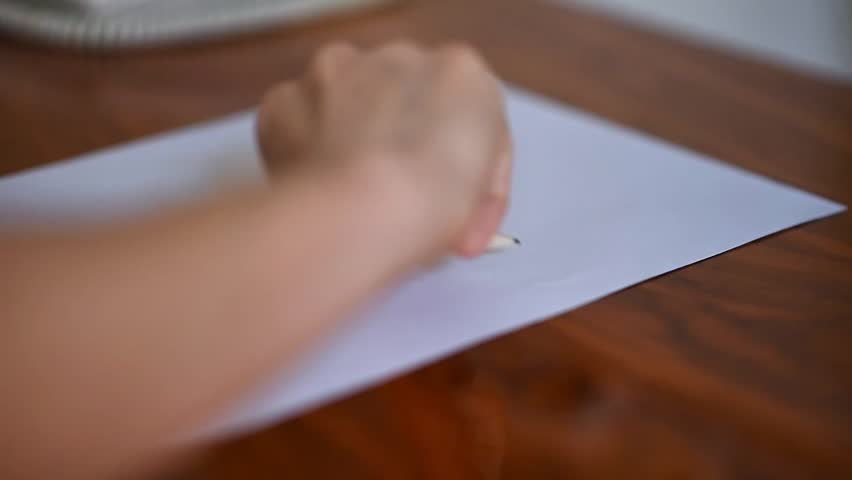 Artist, student, or designer sketching on a white sheet with a pencil on a wooden desk