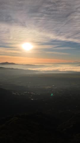 An aerial view of a sunrise seen from the top of a hill, with clouds drifting softly in the background.