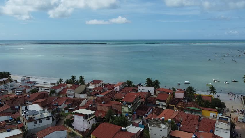 Aerial view of a Brazilian coastal town next to a Caribbean beach with turquoise water and boats sailing in the sea.