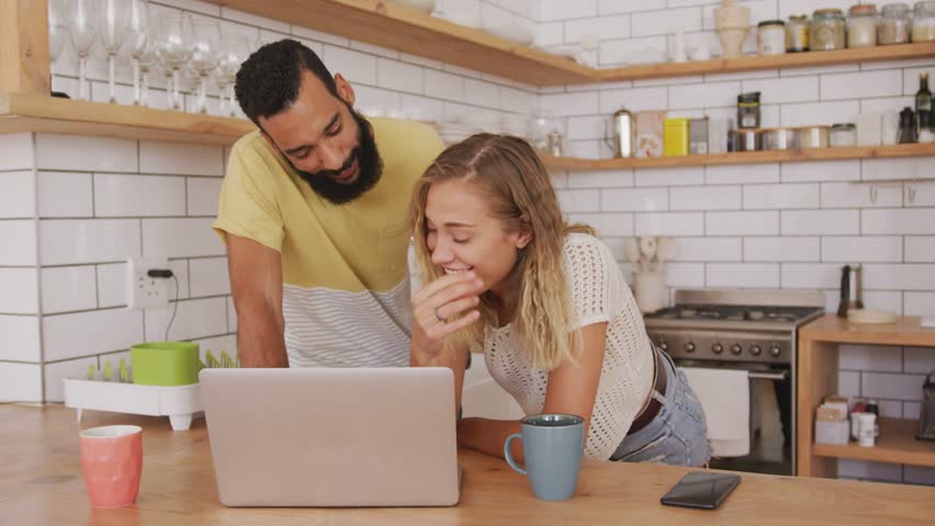 Couple leaning in kitchen viewing laptop and sharing, activating animated lines forming tech burst. Duo, collaboration, countertop, home, device, overlay, casual