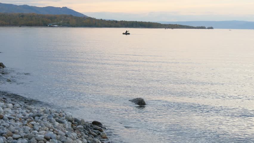 Sunset on Lake Baikal on a cold autumn evening. Fishing boats try to reel in their evening catch. The orange sky is reflected in the calm surface of the lake.