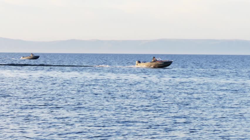 Sunset on Lake Baikal on a cold autumn evening. Fishing boats try to reel in their evening catch. The orange sky is reflected in the calm surface of the lake.