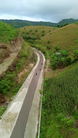 A winding road through green hills with a person riding a motorbike