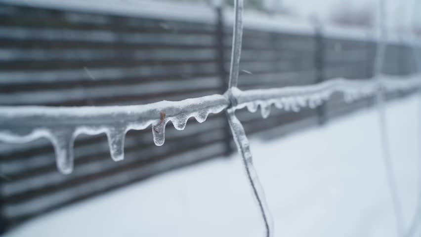 Icicles hanging from frozen wire fence close-up after ice storm in winter