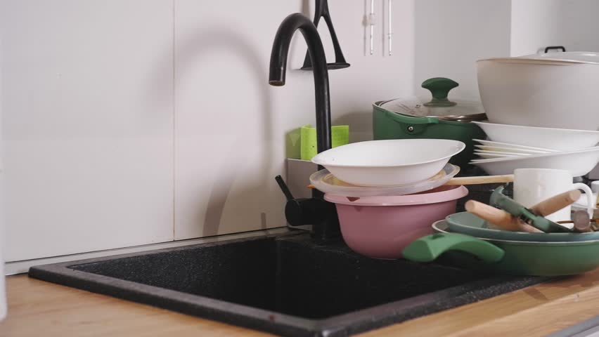 Large pile of unwashed dishes, pans, and cutlery stacked in a modern kitchen sink