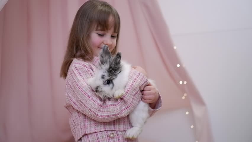 Adorable happy child gently holding and hugging a cute domestic bunny in her arms