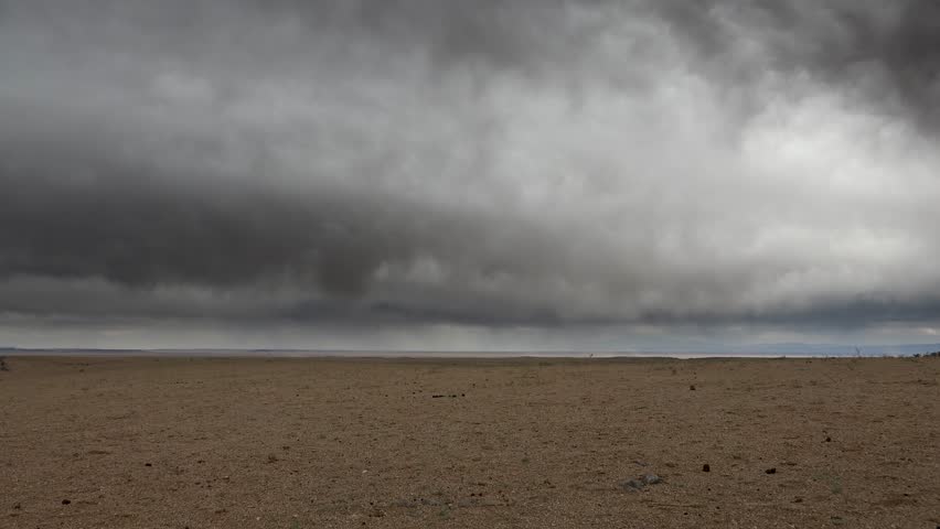 Rain clouds approach Gobi Desert and treeless plains across Central Asia before incoming storm. Dark weather front advances above dryland, bringing rare rainfall to empty wasteland. The incoming storm expands the clip toward weather forecasting, rare desert rainfall, climate contrast, and atmospheric drama over barren land. Clouds over the Gobi show how even dry regions experience sudden meteorological shifts that reshape light, visibility, and terrain mood.