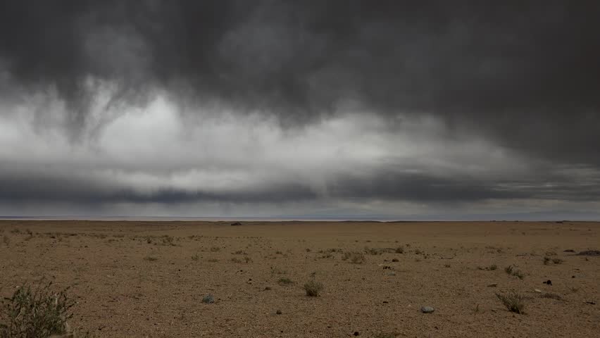 Rain clouds approach Gobi Desert and treeless plains across Central Asia before incoming storm. Dark weather front advances above dryland, bringing rare rainfall to empty wasteland. The incoming storm expands the clip toward weather forecasting, rare desert rainfall, climate contrast, and atmospheric drama over barren land. Clouds over the Gobi show how even dry regions experience sudden meteorological shifts that reshape light, visibility, and terrain mood.