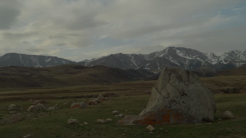 Mountain landscape with a large rock in the foreground and distant snow capped peaks. Natural scenic environment with open valley and calm atmosphere.