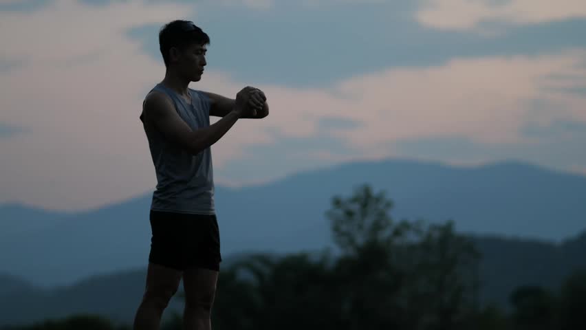 Cinematic shot of a male athlete standing and using a smartphone to take a photo of beautiful mountains during blue hour, outdoor lifestyle and technology concept