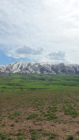 Vertical scenic view of a mountain meadow under a cloudy sky.