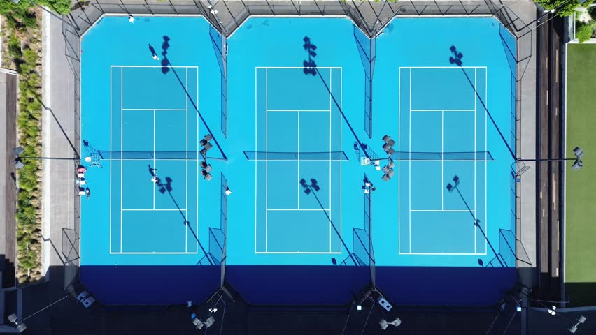 Melbourne, Victoria, Australia – 17th April 2026: Aerial top-down view of multiple blue tennis courts with players and shadows in sports precinct