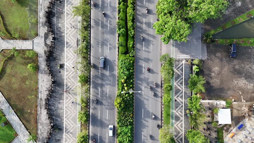 A view from above of an urban boulevard with a green median, traffic, and pedestrians along the sidewalk in a park in the city of Pontianak, Indonesia