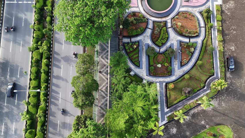 A view from above of an urban boulevard with a green median, traffic, and pedestrians along the sidewalk in a park in the city of Pontianak, Indonesia