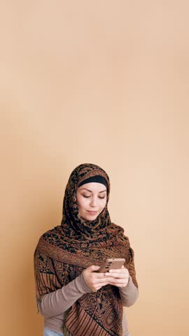 Beautiful muslim woman in traditional clothing smiling while using a mobile phone. Middle eastern female enjoying online communication. Vertical