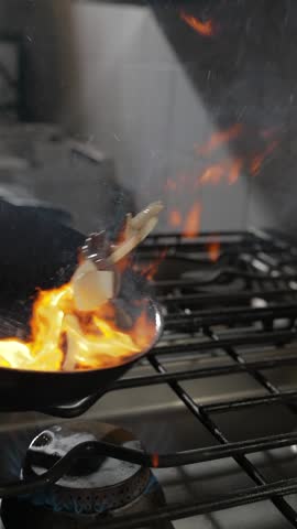 Flying Asian Meal with Meat in Wok on Opened Fire. Slow Motion Vertical Shot. Blur Kitchen Interior on Background. 