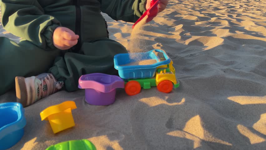 Child playing with small toy car on sandy beach. Kid engaged in fun outdoor activity on summer day. Plastic vehicle model moving through sand dunes at seaside.