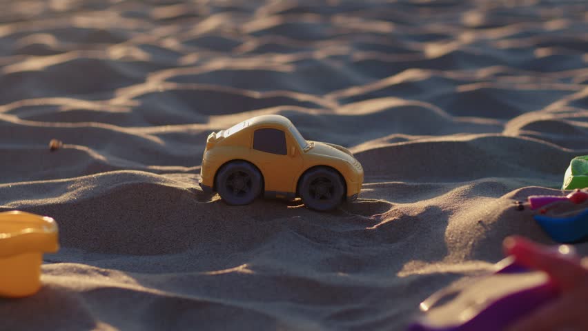 Child playing with small toy car on sandy beach. Kid engaged in fun outdoor activity on summer day. Plastic vehicle model moving through sand dunes at seaside.