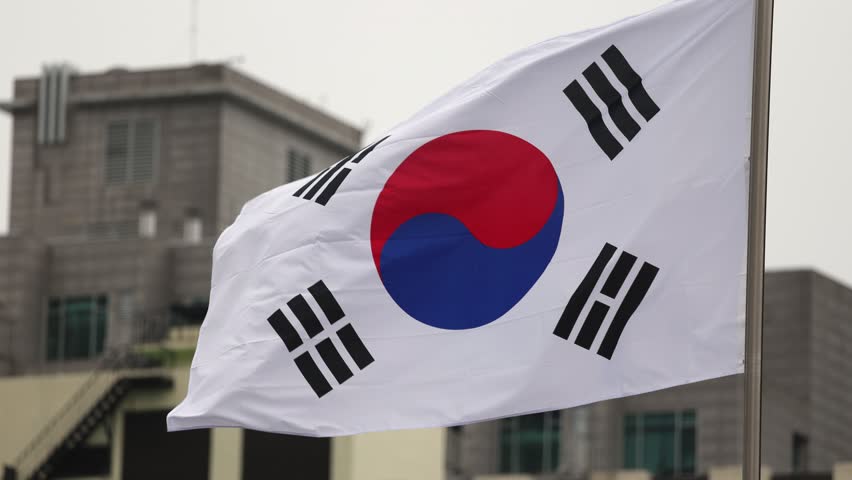 Taegeukgi flag waving, representing South Korea, with urban buildings in the background