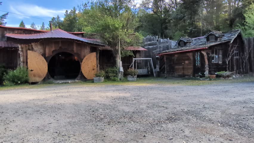 Video of whimsical building with round doorway, gravel lot, swing and nearby log cabin, highlighting imaginative roadside architecture in southern Oregon.