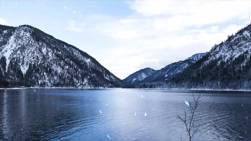 Gentle snowfall beginning over a partly frozen lake in winter. Soft white snowflakes falling on icy blue water and thin ice crust.