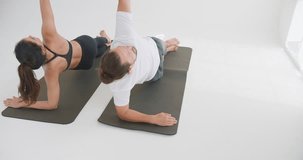A couple practices a synchronized side plank yoga pose on mats in a bright studio, focusing on core strength and balance to promote a healthy lifestyle. - Powered by Shutterstock - Get 15% off with code: PIKWIZARD15