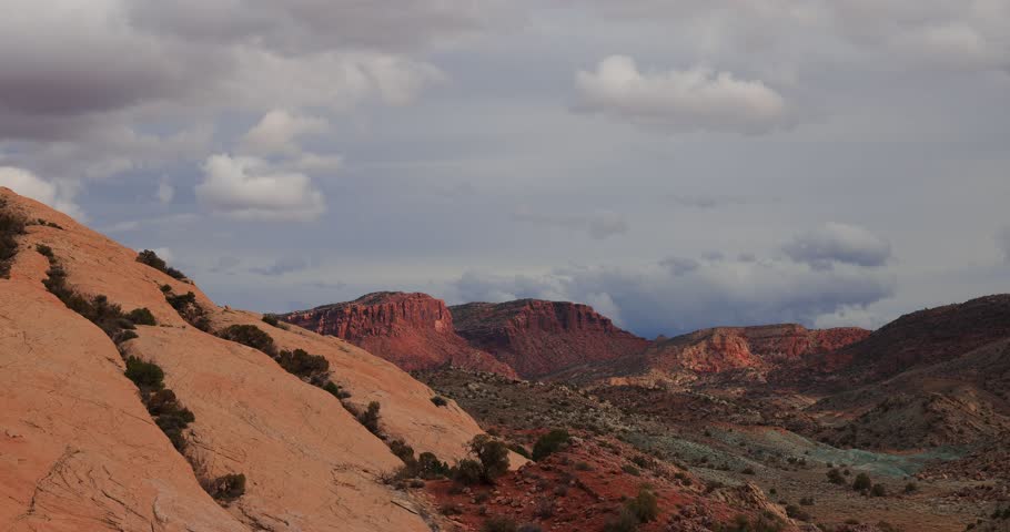 Sunlight fades across rust-colored canyon walls as rolling clouds drift over the horizon, casting long shadows onto the desert terrain below.