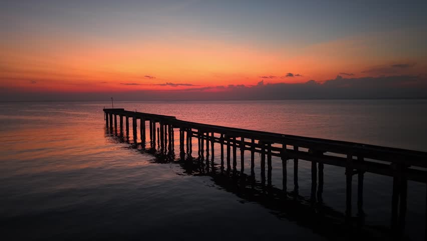 Aerial drone view of Segenting jetty at dramatic orange sunset over calm Malaysian sea.