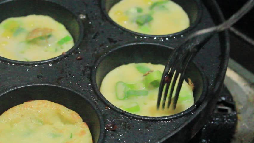 Cooking mini omelets with green onions in a traditional round mold pan.