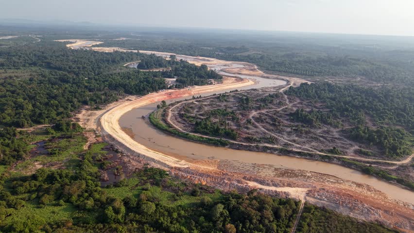 River curves through cleared forest. Brown water flows beside barren land. Trees still stand far beyond the cut
