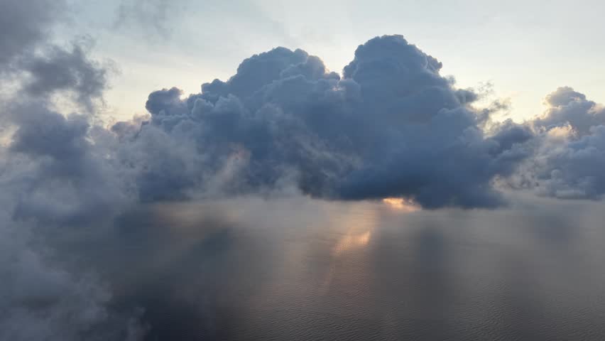 Dark clouds dominate the sky. Sunlight breaks through the upper clouds. Warm light illuminates the mist below