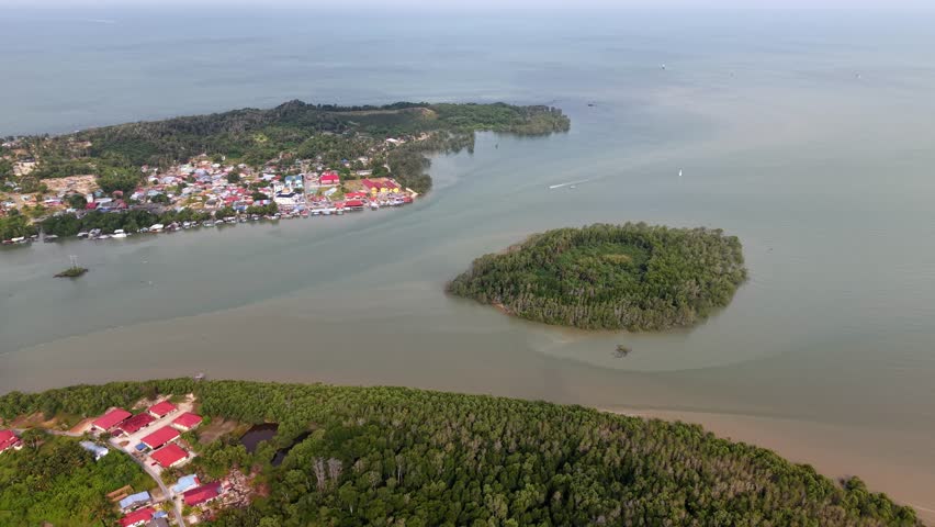 Aerial view of coastal islands with lush greenery. Muddy waters separate verdant islets from a small village at Sedili Besar town