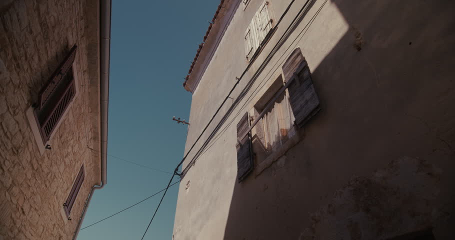 A historic building facade with wooden shutters and overhead cables is viewed from below in a narrow street.