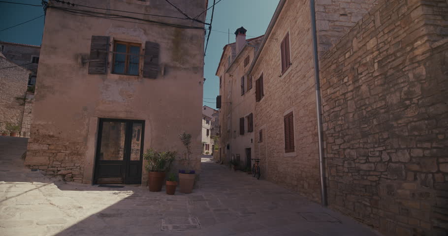 A stone street intersection with historic buildings, potted plants, and a bicycle is shown.