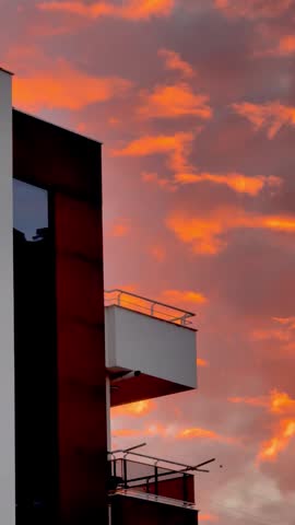 Amazing vibrant orange sky with dramatic clouds during intense sunset. Silhouettes of a power tower, residential buildings, mountains against glowing sky. Focuses on the "wow" effect. Evening dusk. 