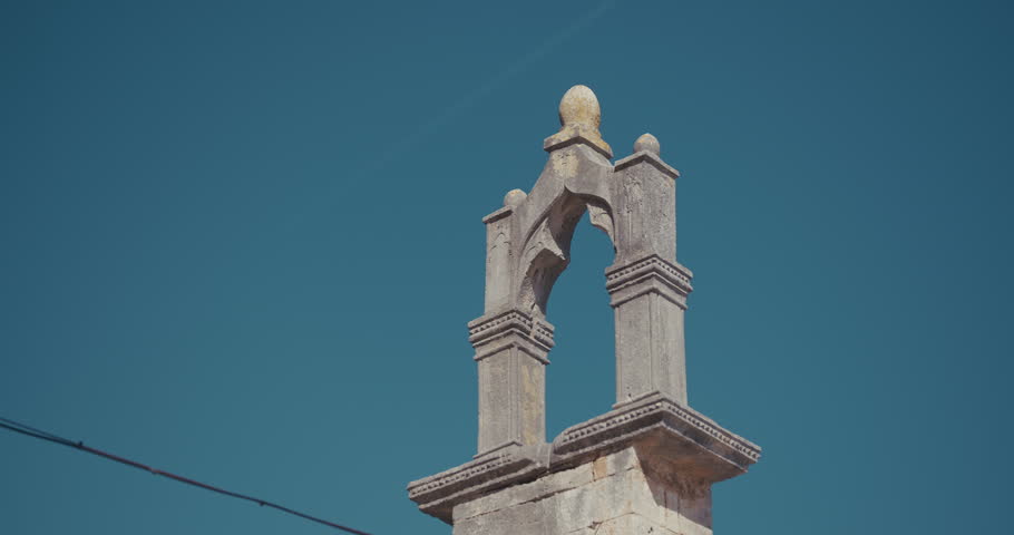 A stone bell gable on top of a small chapel is shown against a clear sky.