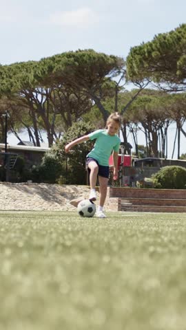 Child in teal shirt entering grass, coming to ball, using soft touches, kicking, training control. Soccer, dribble, teammates, outdoor, park, playground, vertical video