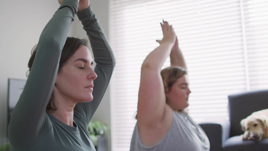 Two women doing breathwork at home, guided cue starting green-yellow-blue lines over hands for calm. Meditation, duo, serene, mindfulness, yoga, livingroom, naturallight