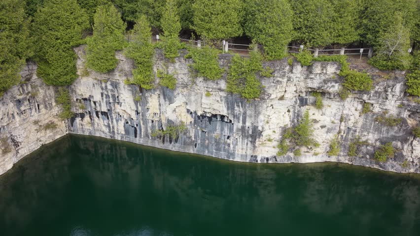 A wide aerial shot of the historic Elora Quarry Conservation Area in Ontario, showcasing its two-acre emerald swimming hole encircled by dramatic 12-meter limestone cliffs and dense forest