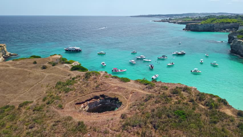 Aerial view of Grotta Sfondata sea cave on the Salento coast. The broken limestone roof reveals a turquoise lagoon with crystal clear water near Otranto during a sunny summer in Italy.