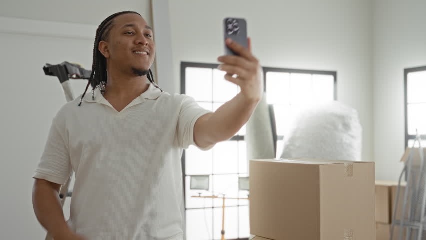 Man holding smartphone, hand raised, taking a quick selfie in an apartment building; new home confidence.