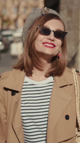 A Chic Woman Dressed in a Striped Top and Stylish Sunglasses Walking Outdoors in the Sun