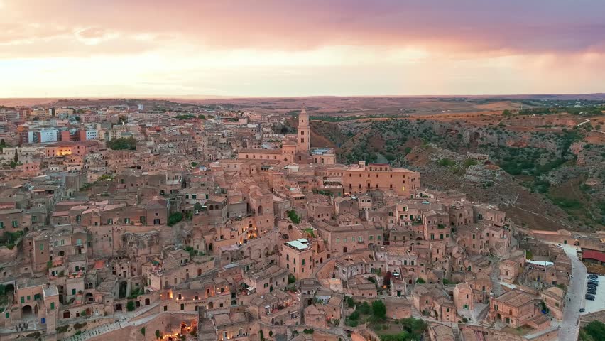 Drone view of Matera at sunset, Basilicata, Italy. The golden hour light illuminates the Cathedral of Maria Santissima of the Bruna and the historic Sassi dwellings across the ancient skyline of.