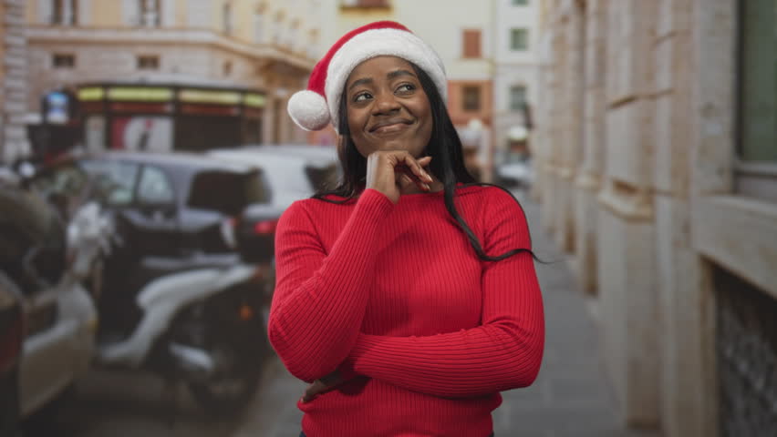 Woman wearing santa hat rests chin on hand in hand on chin gesture on a street with parked scooters and cars; festive cheer.