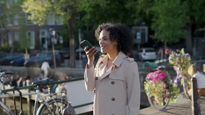 Elegant businesswoman recording a voice message on her smartphone while visiting amsterdam, netherlands on a sunny day