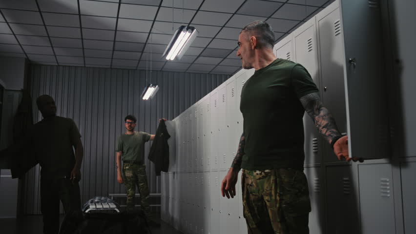 Group of Soldiers in Military Uniforms Gathers in Base Locker Room, Relaxed Conversation, Preparing Equipment, and Adjusting Gear Before Upcoming Mission. Daily Routine and Camaraderie in Army.