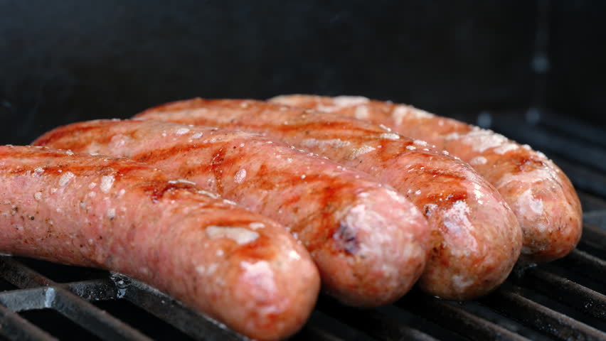 View of juicy meat sausages grilling on barbecue with open flame. Close up of juicy meat cooking on grill, outdoor food and summer barbecue