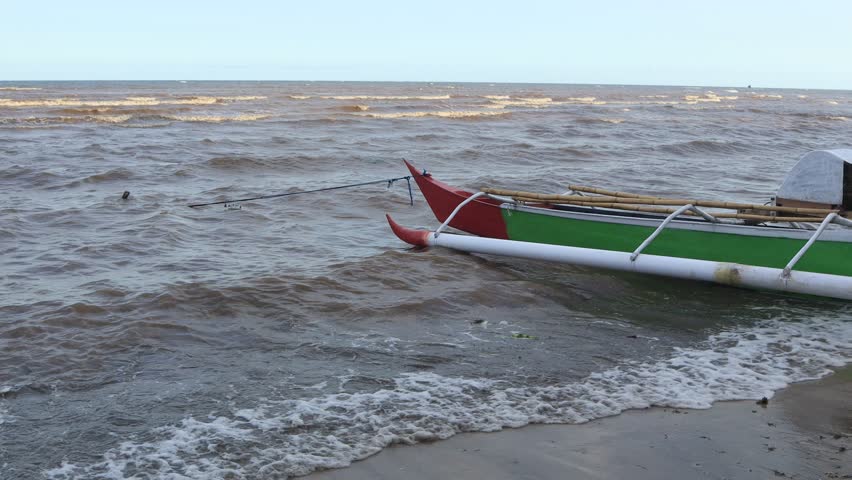 Small waves move slowly on the beach, fishing boats on the shore