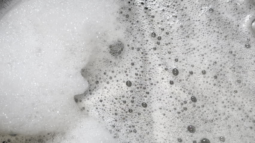Soap suds jiggle and swirl in kitchen sink, creating an abstract background plate and graphic element of soap suds and bubbles. 
