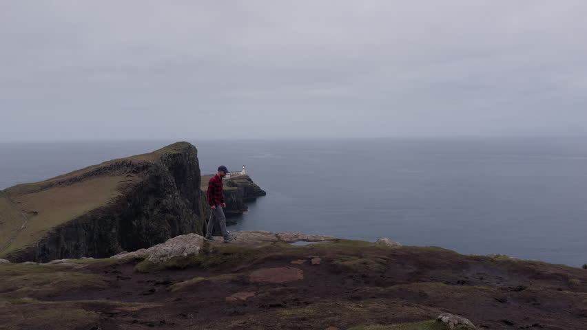 A man walking on the edge of a mountain, Neist Point Lighthouse on Isle of Skye overlooking the Atlantic Ocean, Scotland
